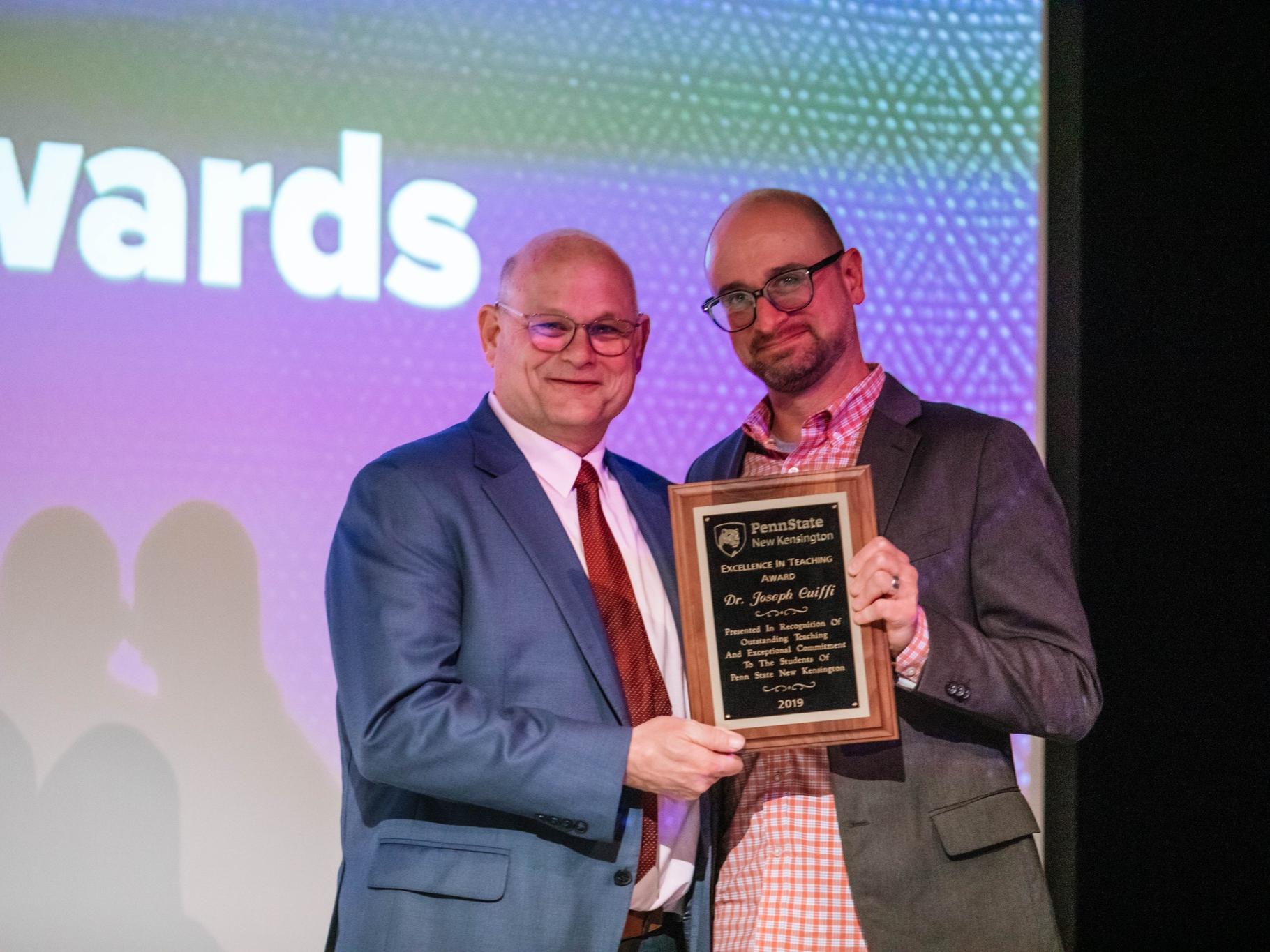 Two people stand holding a plaque