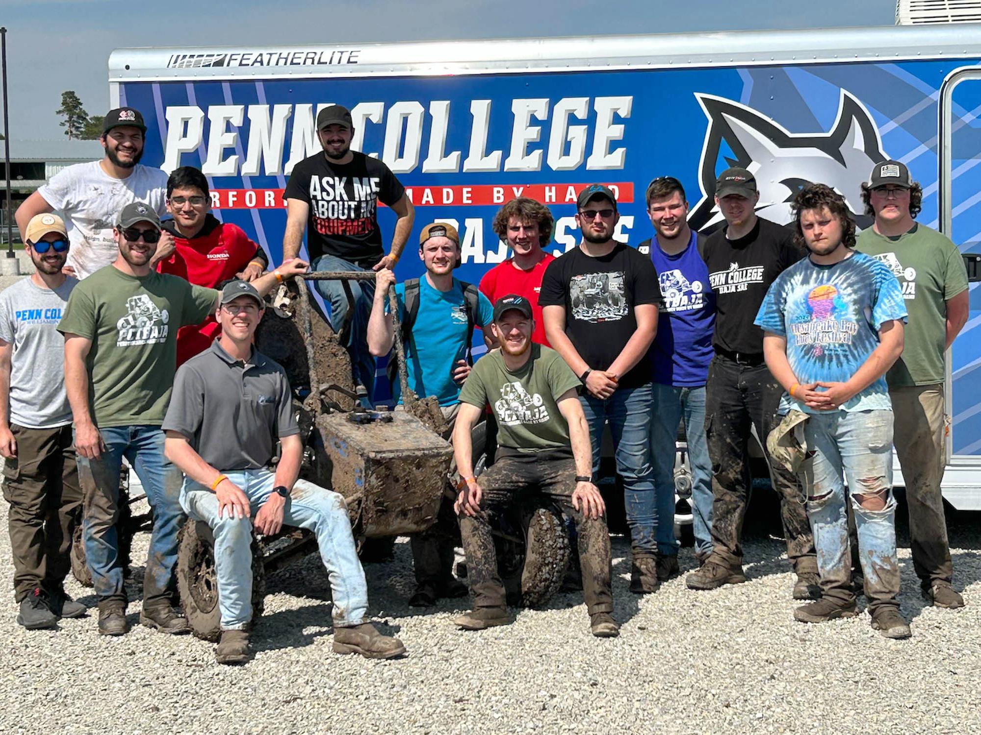 A group of people stand in front of a sign that says Penn College