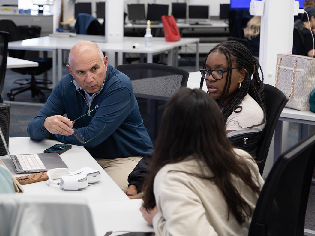 Rob Banas, seated at left, speaking with students Sara Dias and Naomi Were, seated at right.