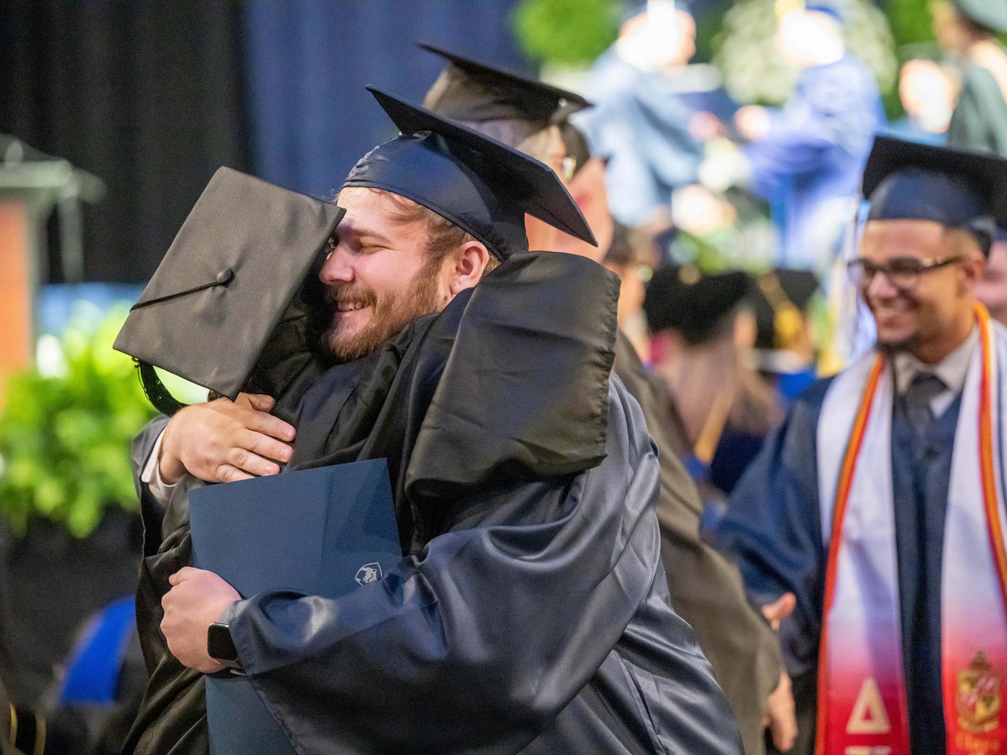 A new graduate hugs a faculty member after leaving the stage at Penn State Behrend's spring 2023 commencement ceremony.