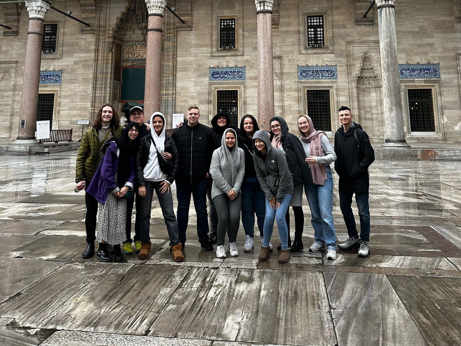 Students gathering with faculty and guests in front of the beautiful Turkish architecture. 