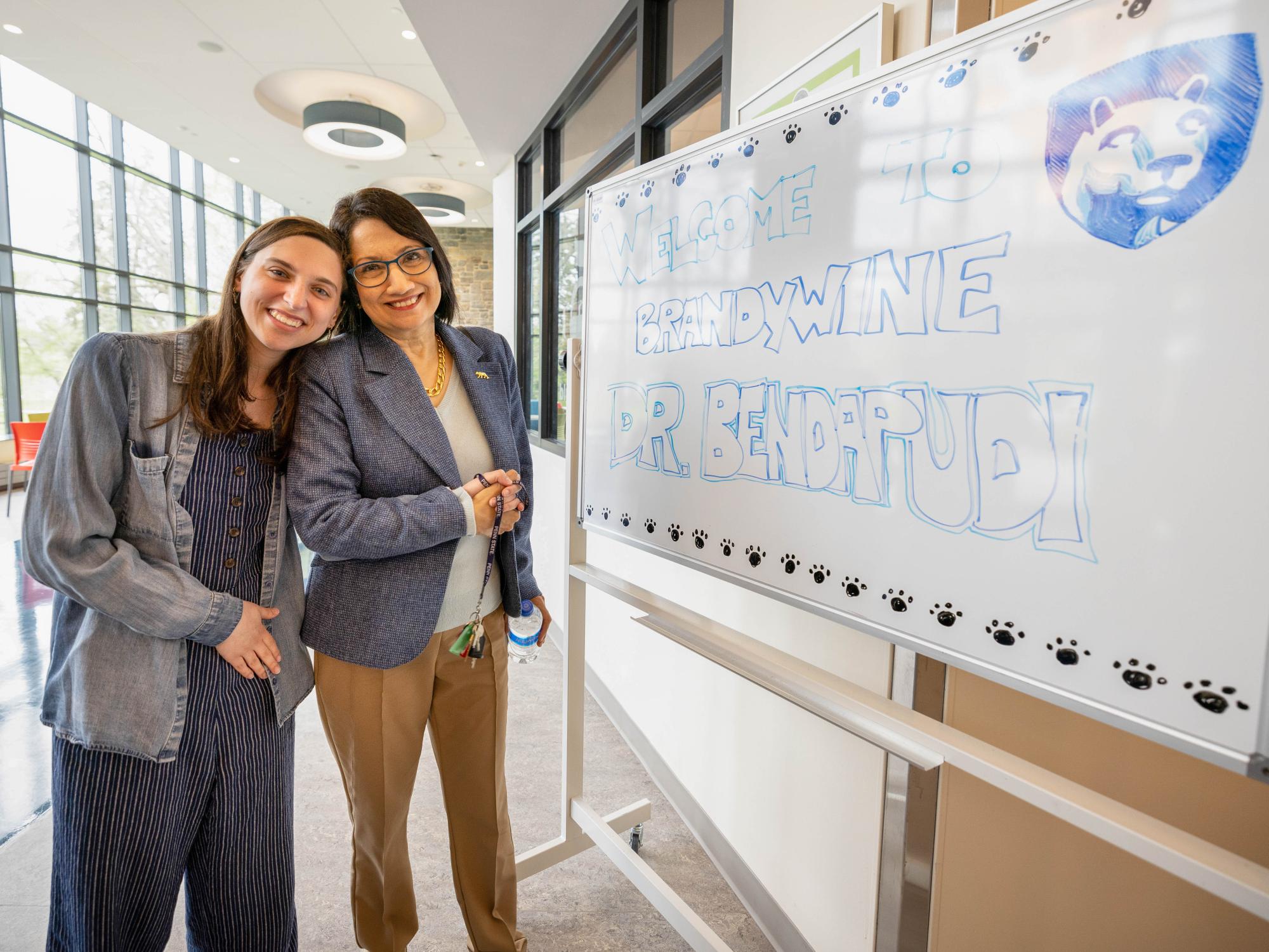 Two women stand next to each other in front of a whiteboard.