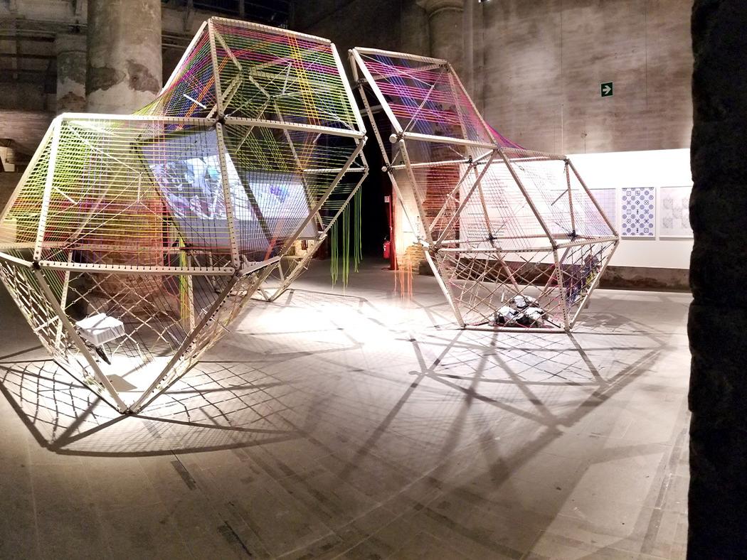 Four bamboo structures are set up with screens projecting images of people working together.