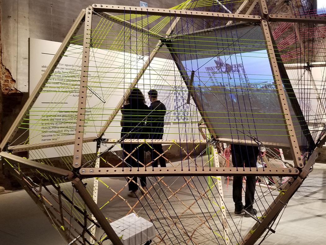 A closeup of a bamboo architectural structure with people viewing text on the wall in the background.