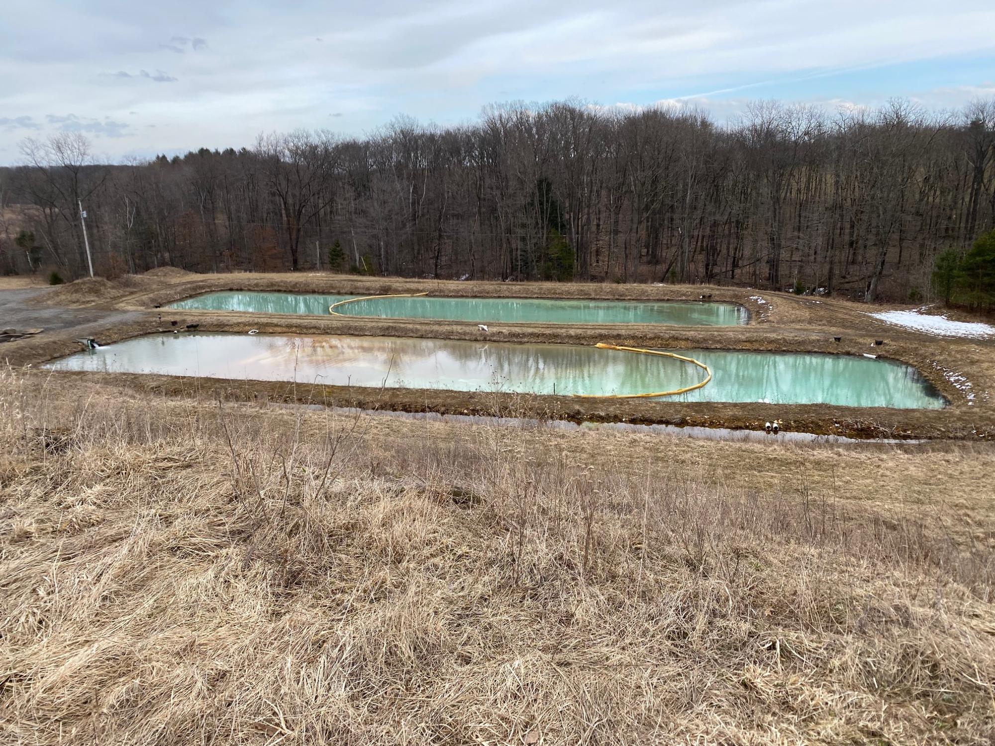 Rectangular sludge pond on brown farm land in front of trees