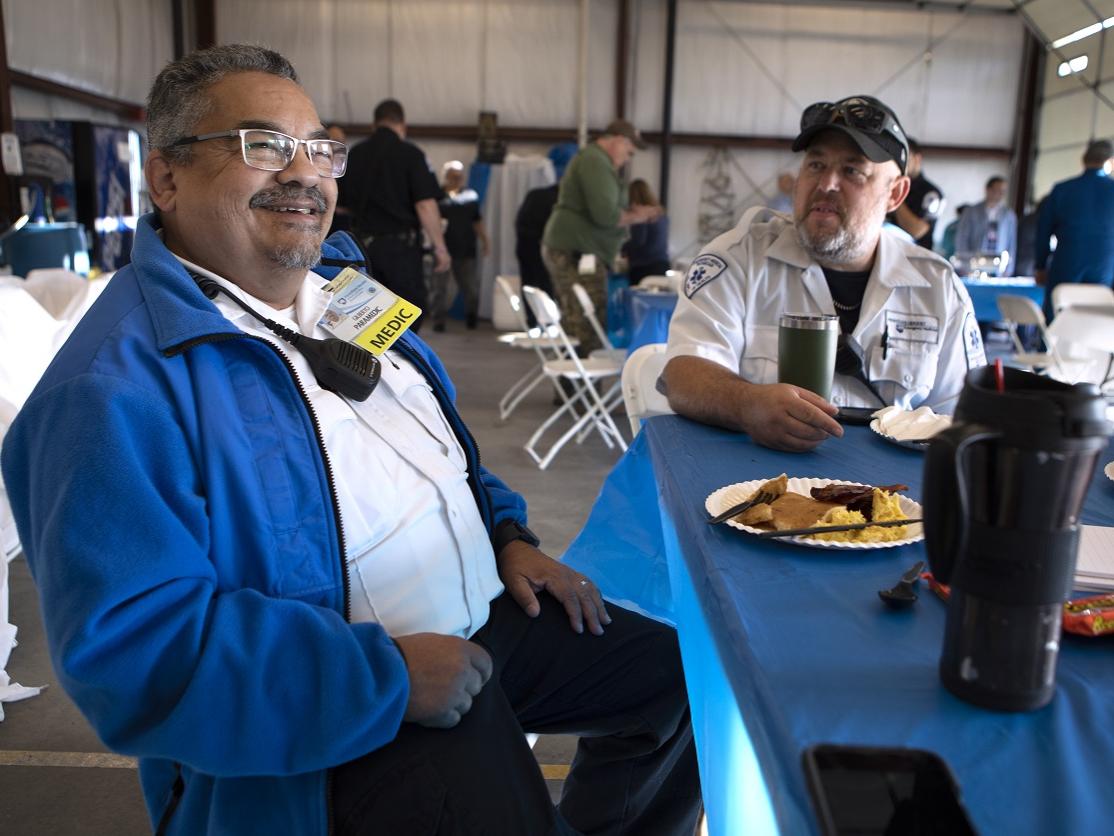 A man seated at a table with a plate of pancakes smiles.