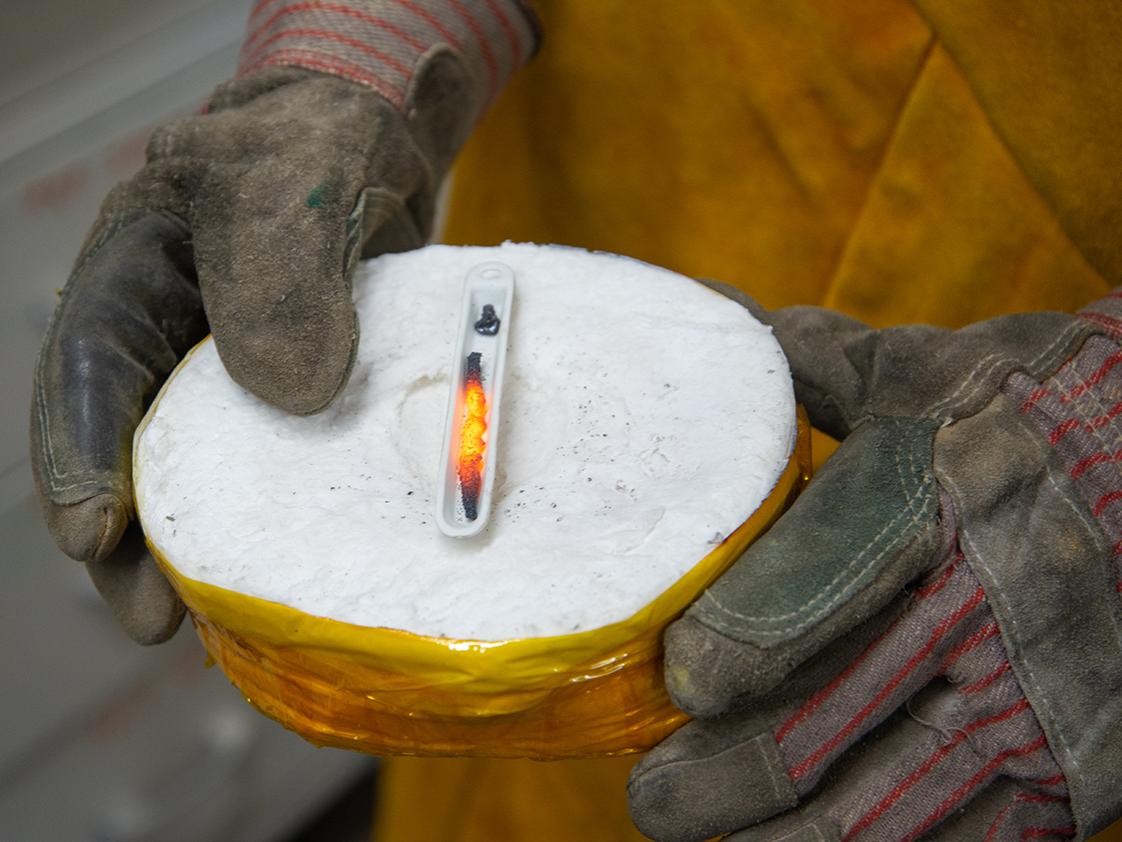 An individual holds a sample of red hot metal in a small circular chamber. 