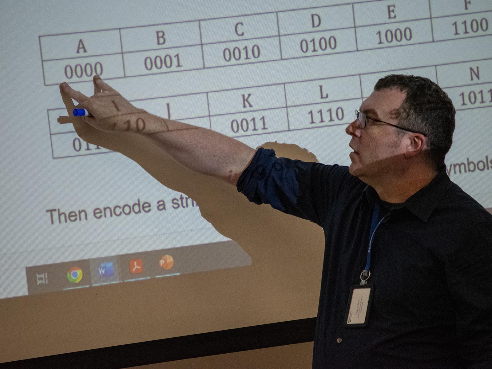 Craig Culbert, assistant teaching professor of mathematical sciences at Penn State Harrisburg, points to information on a large screen.  