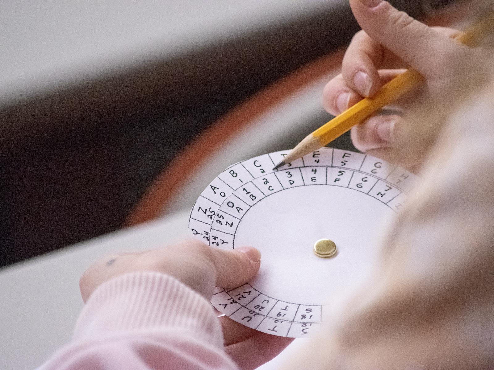 Closeup of a student's hands holding a pencil and a paper wheel with letters and numbers