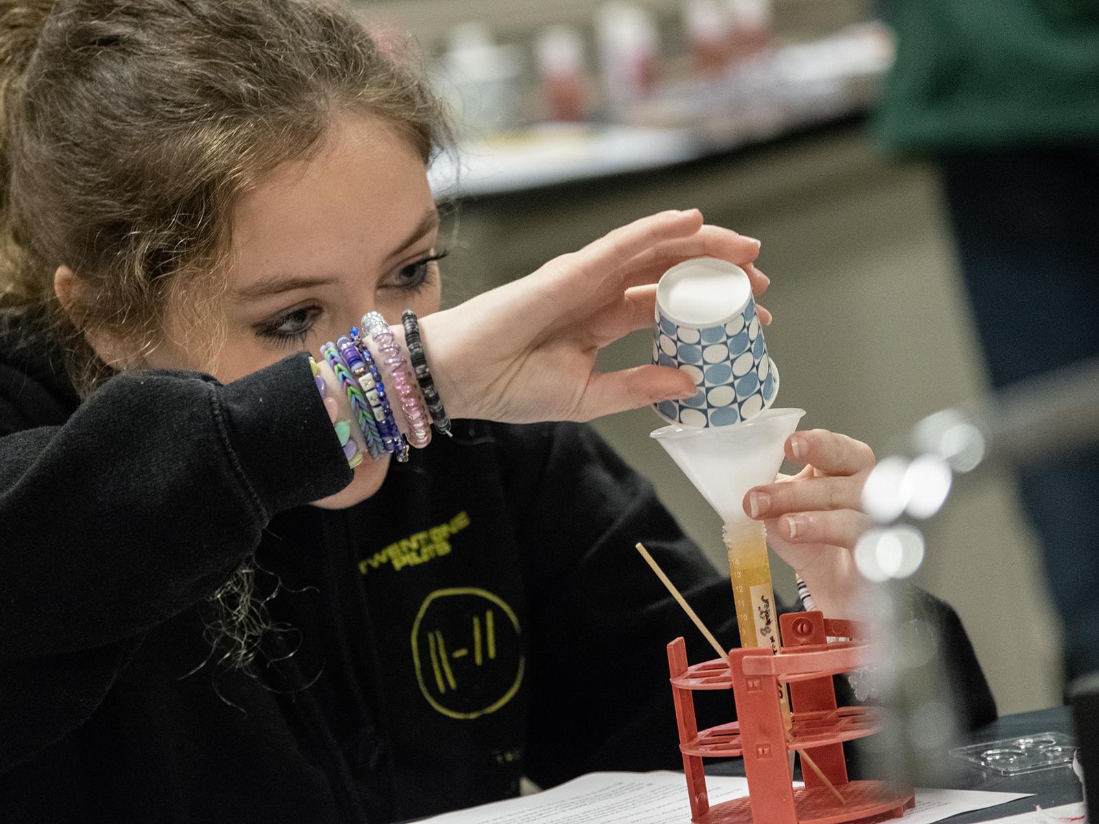 A student pours liquid into a test tube from a small paper cup