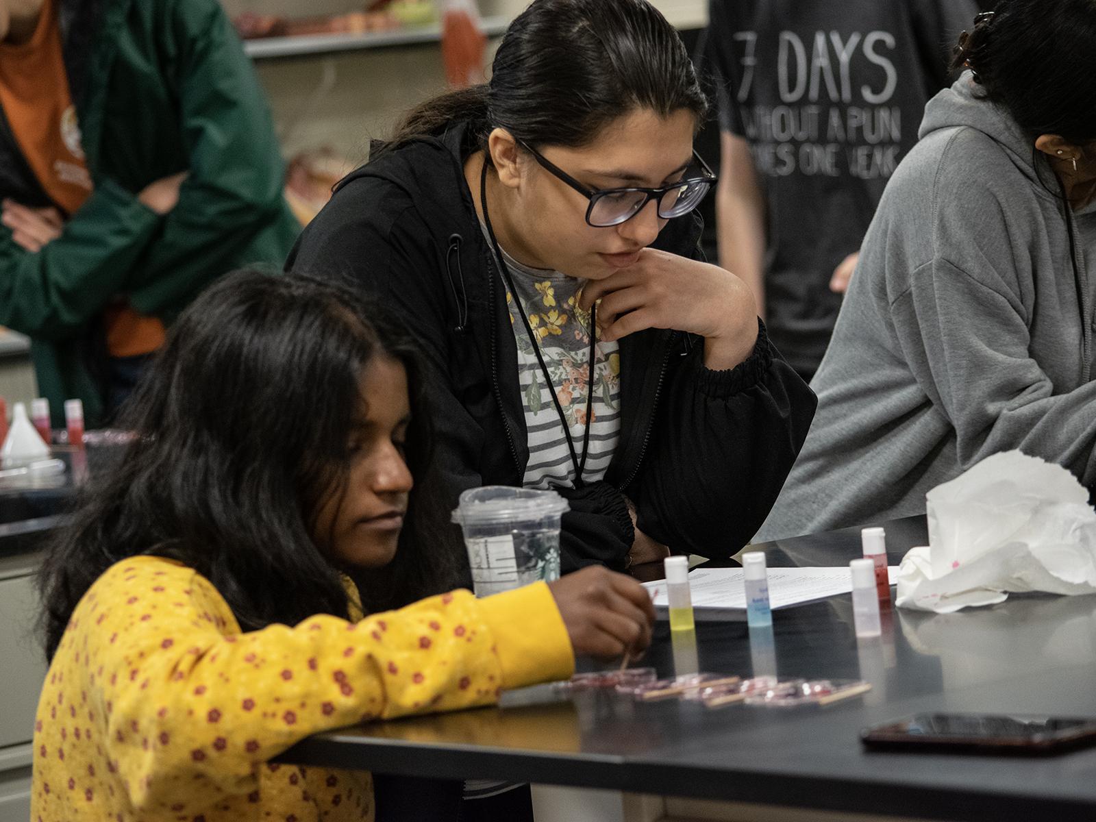 Students work at a lab table with small bottles of liquid
