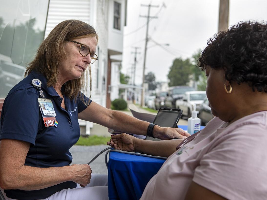 Two women talk while seated at a table on a residential street.