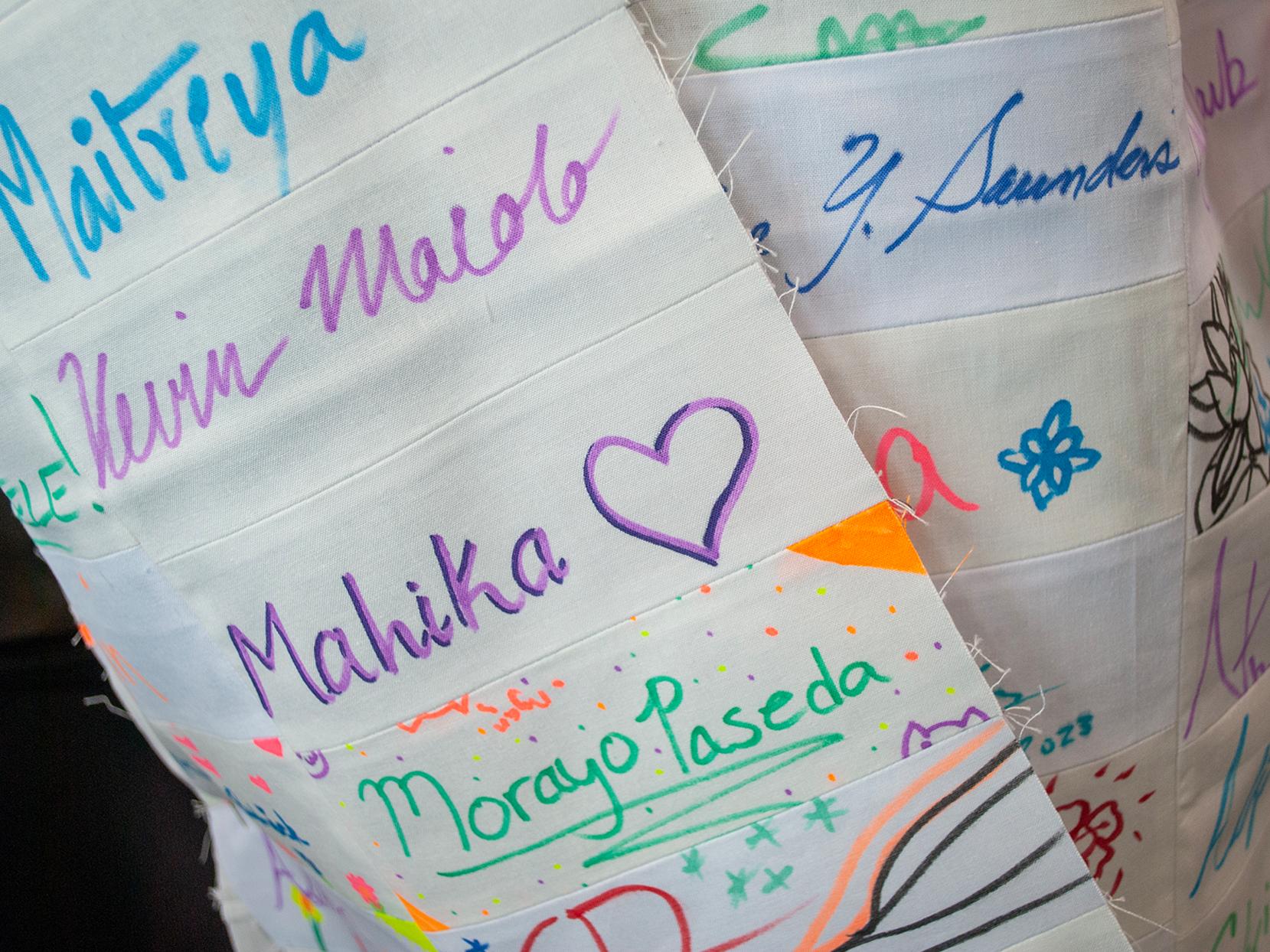 A closeup of Emily Pettet's signature coat in progress - white cloth squares with signatures in bright colors