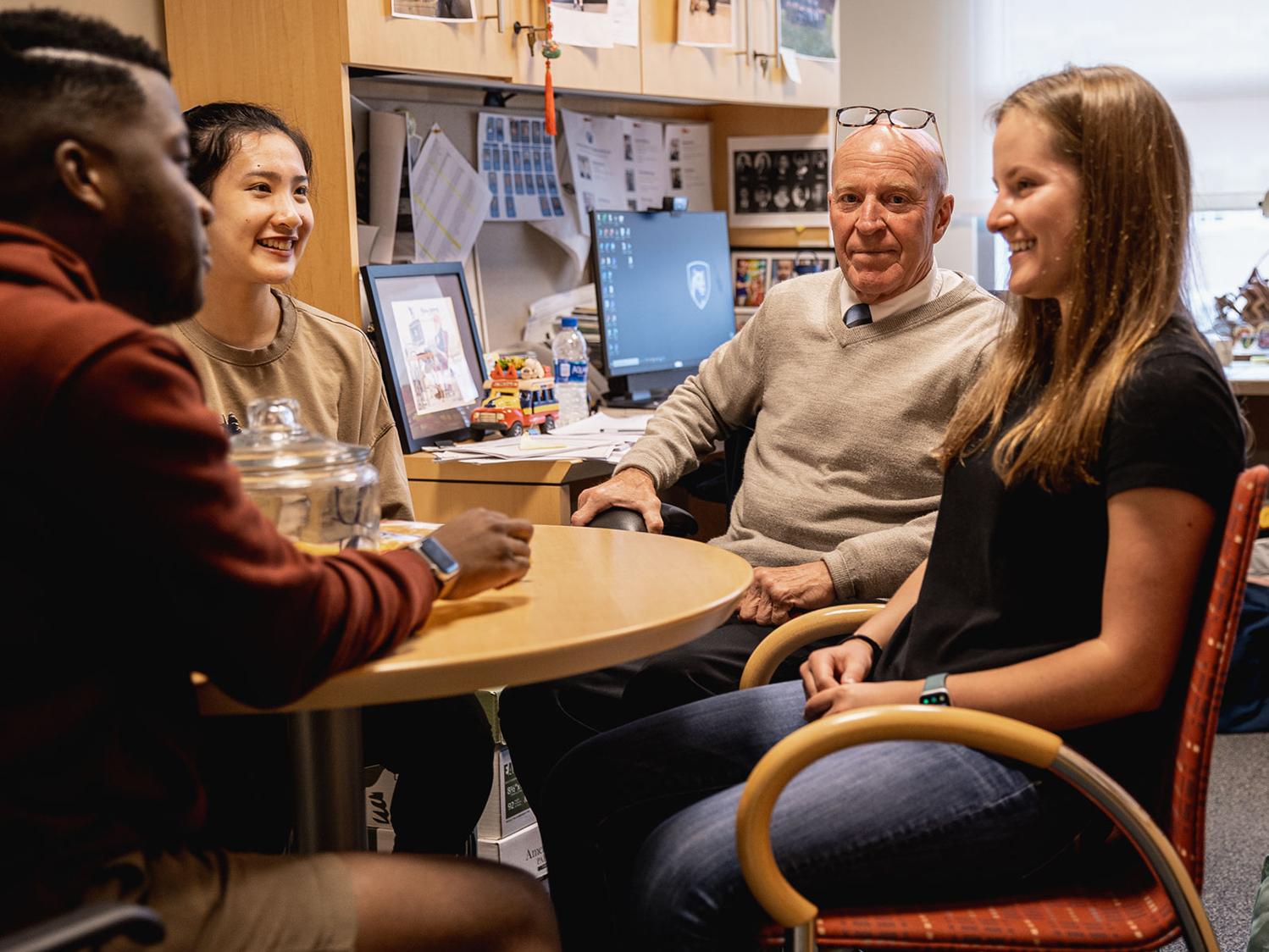 A photo of Bob Novack with students at the table in his office.