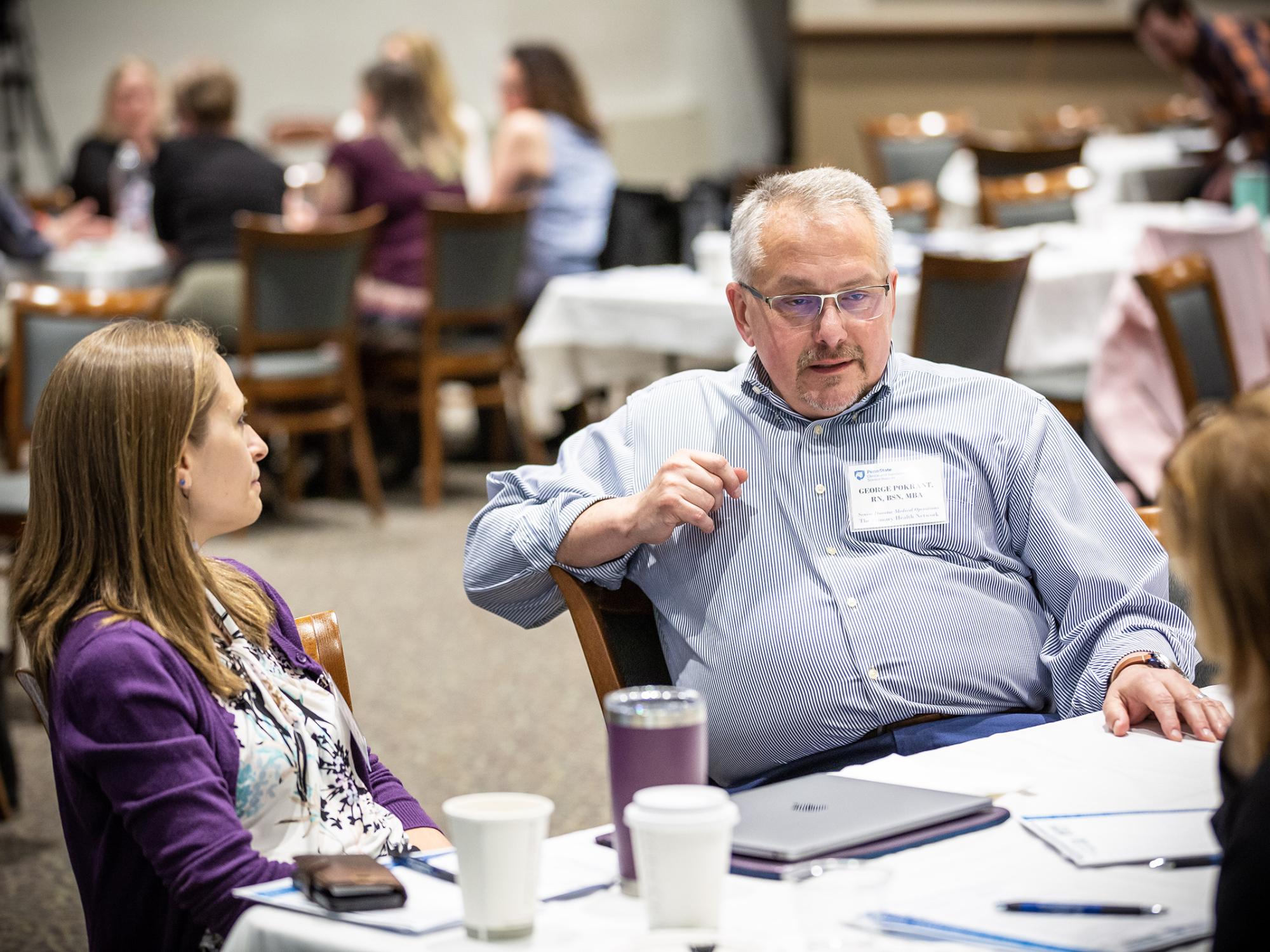 Two people seated at a table have a conversation at a conference.