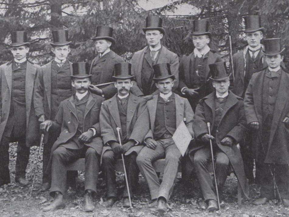 A black and white photo of a group of men dressed in long jackets and top hats