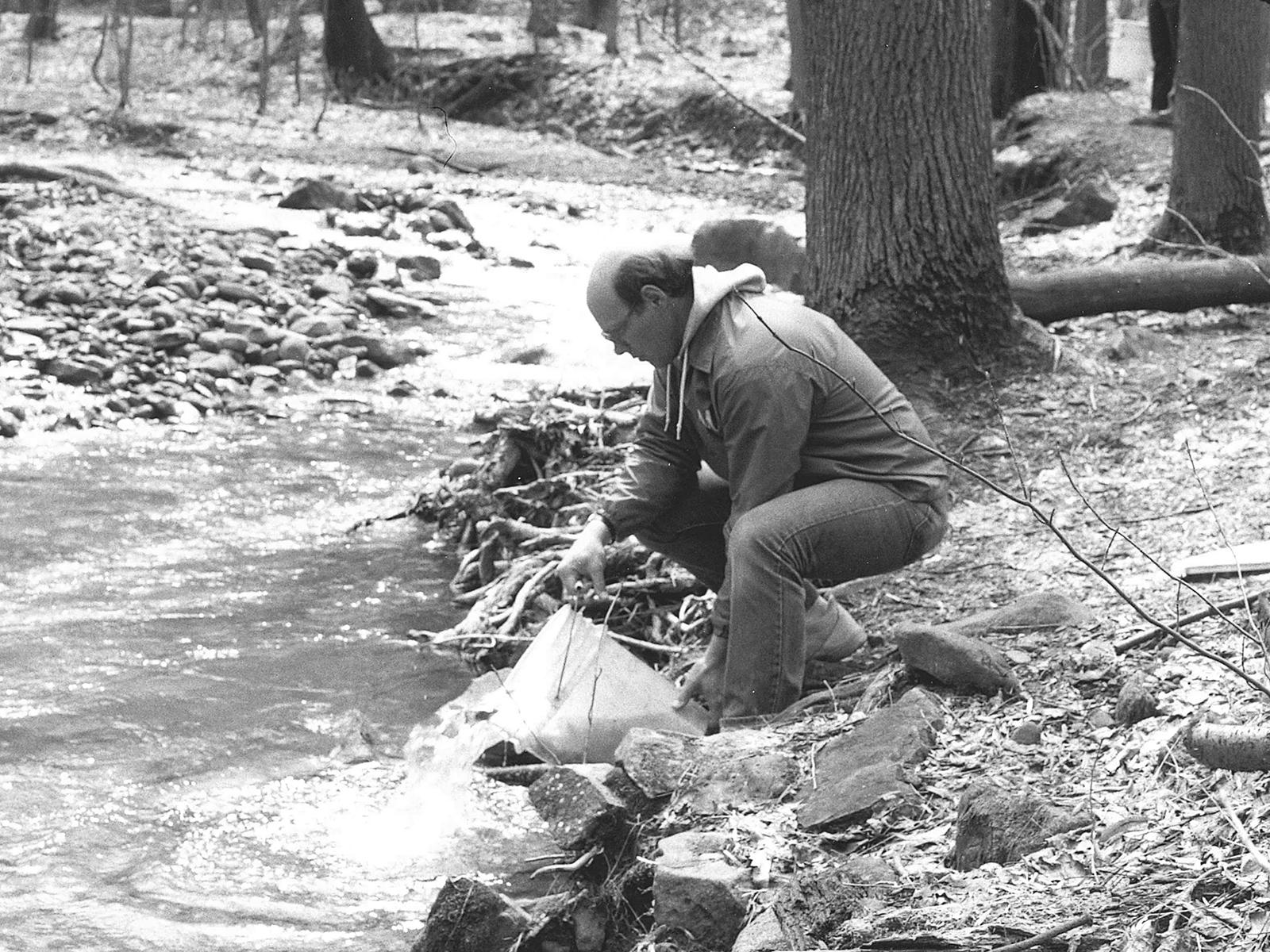 man pouring bucket of liquid into stream