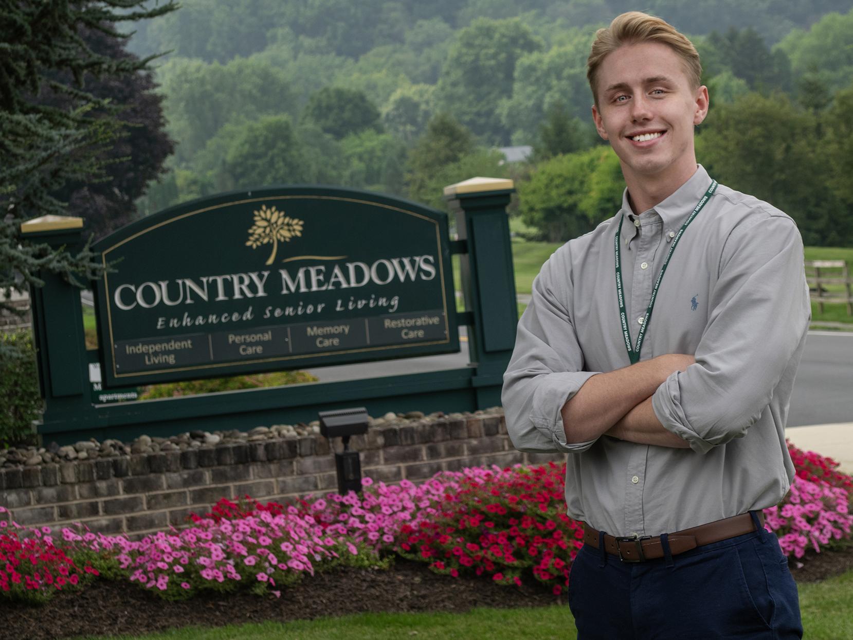 Brennan Quigley stands in front of a sign for Country Meadows