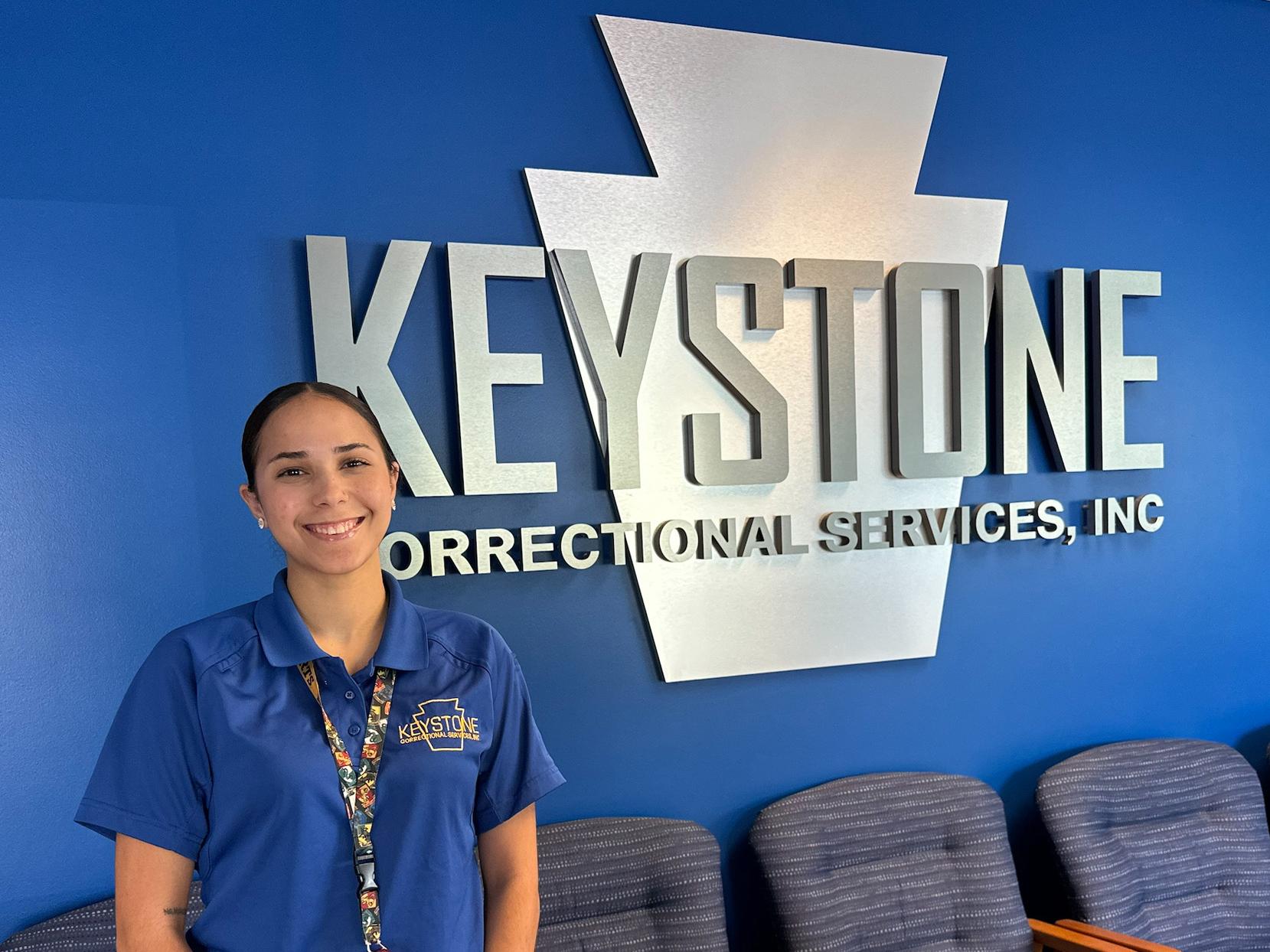 Keys Rodriguez stands in front of a wall with the Keystone Correctional Services logo