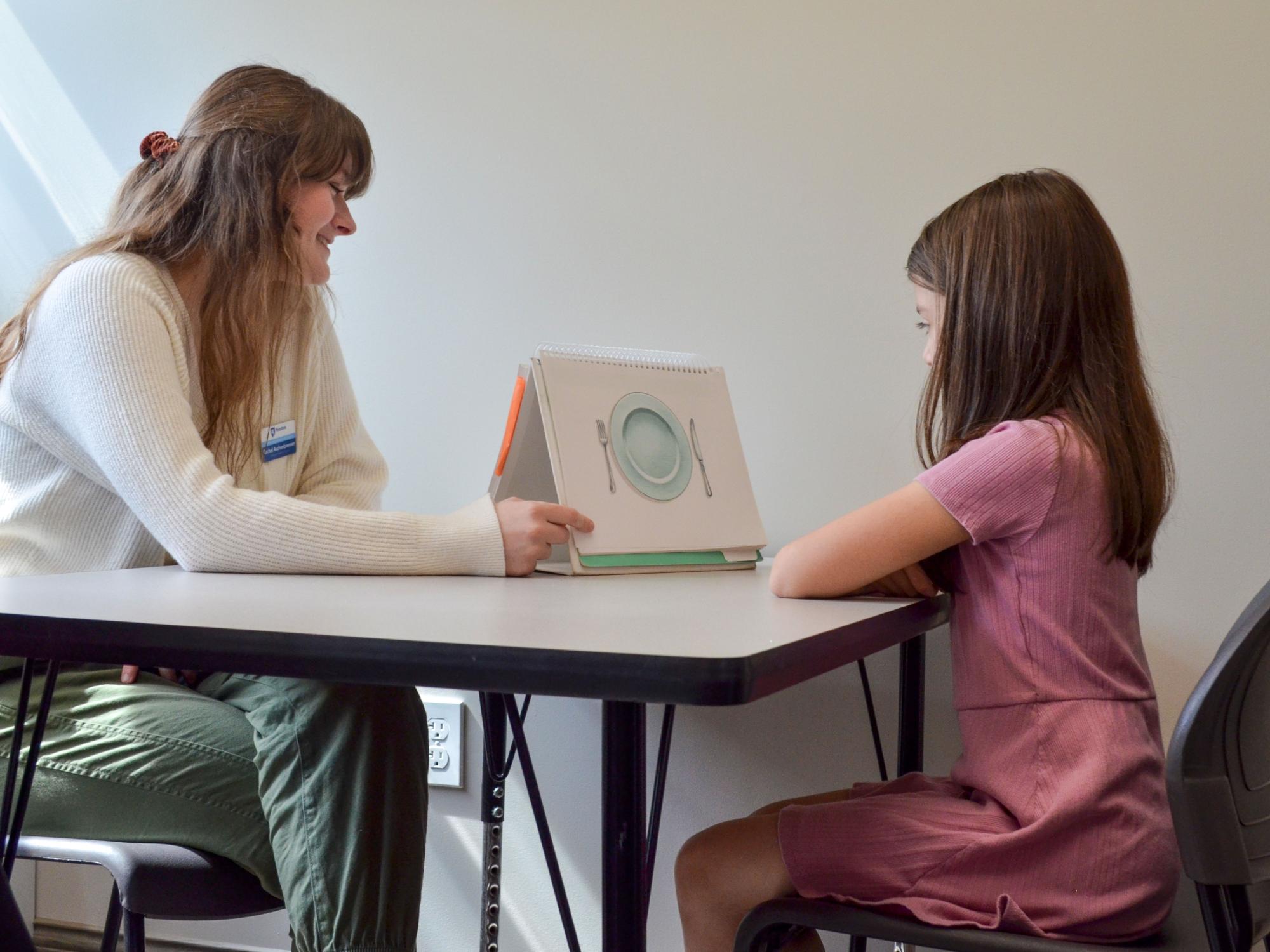 young girl and a speech language pathologist looking at a visual aid