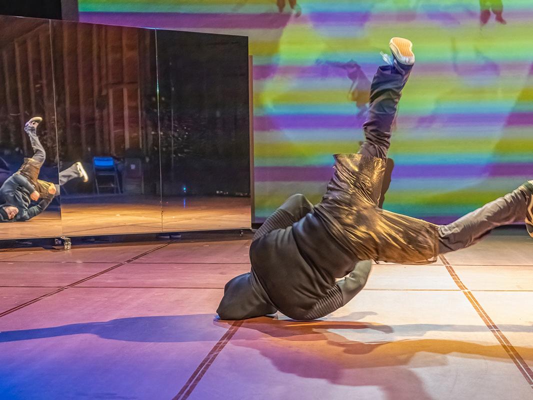 A breakdancer wearing a hoodie balances on his head and shoulder as he spins his legs in the air.