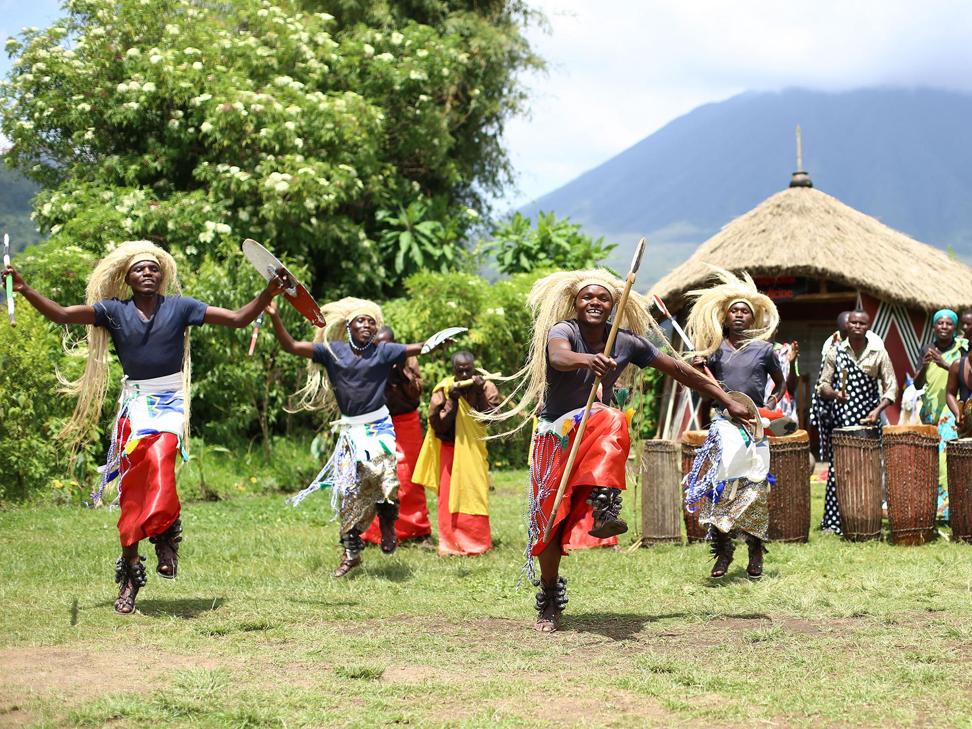 traditional Rwandan dancers outside in front of a hut with a mountain in the background