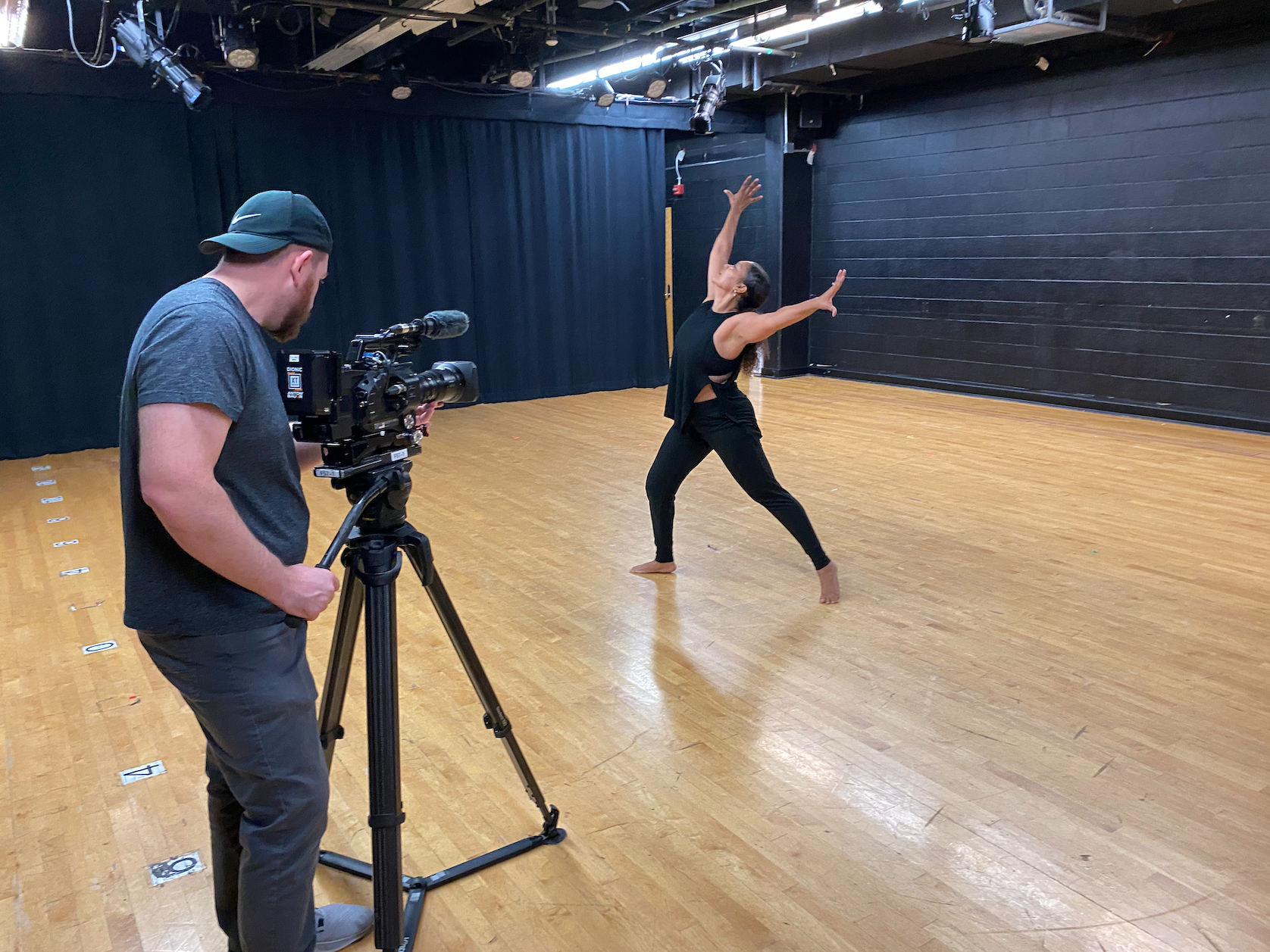 A videographer films a dancer in motion in a studio.