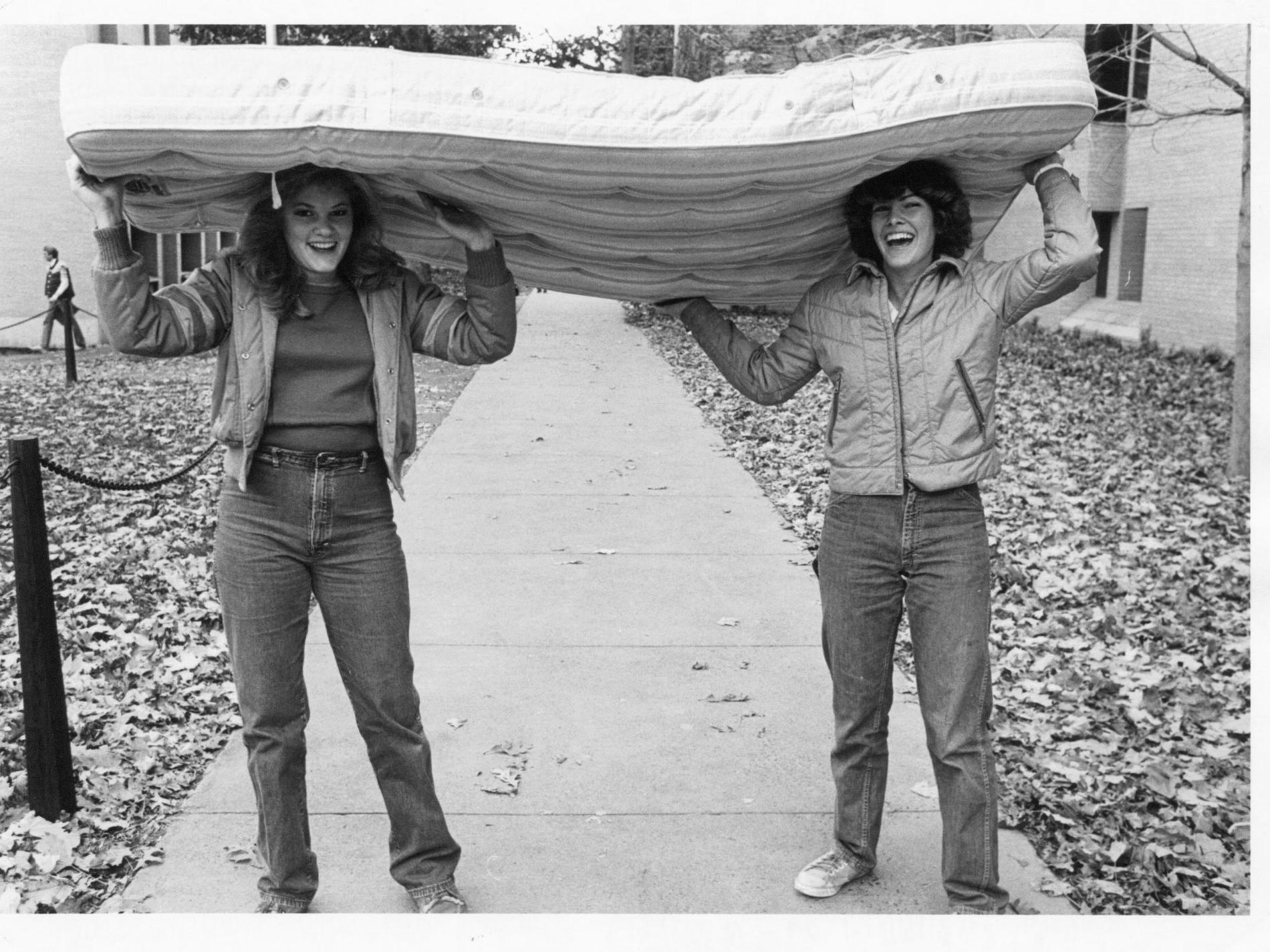 Two female students carry a mattress on their heads