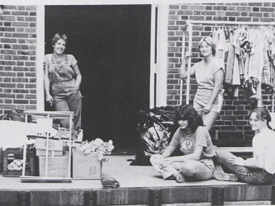 Four female students stand outside a dorm with their belongings