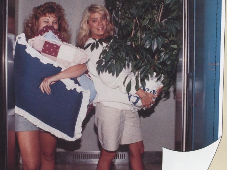 Two female students carry their belongings in a dorm common area on move in day