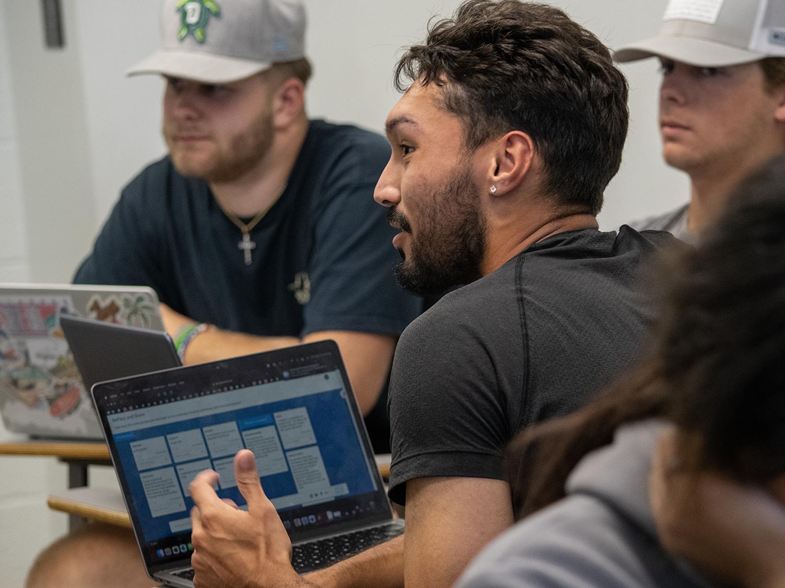 Three students sitting around laptops discuss their experience with virtual reality