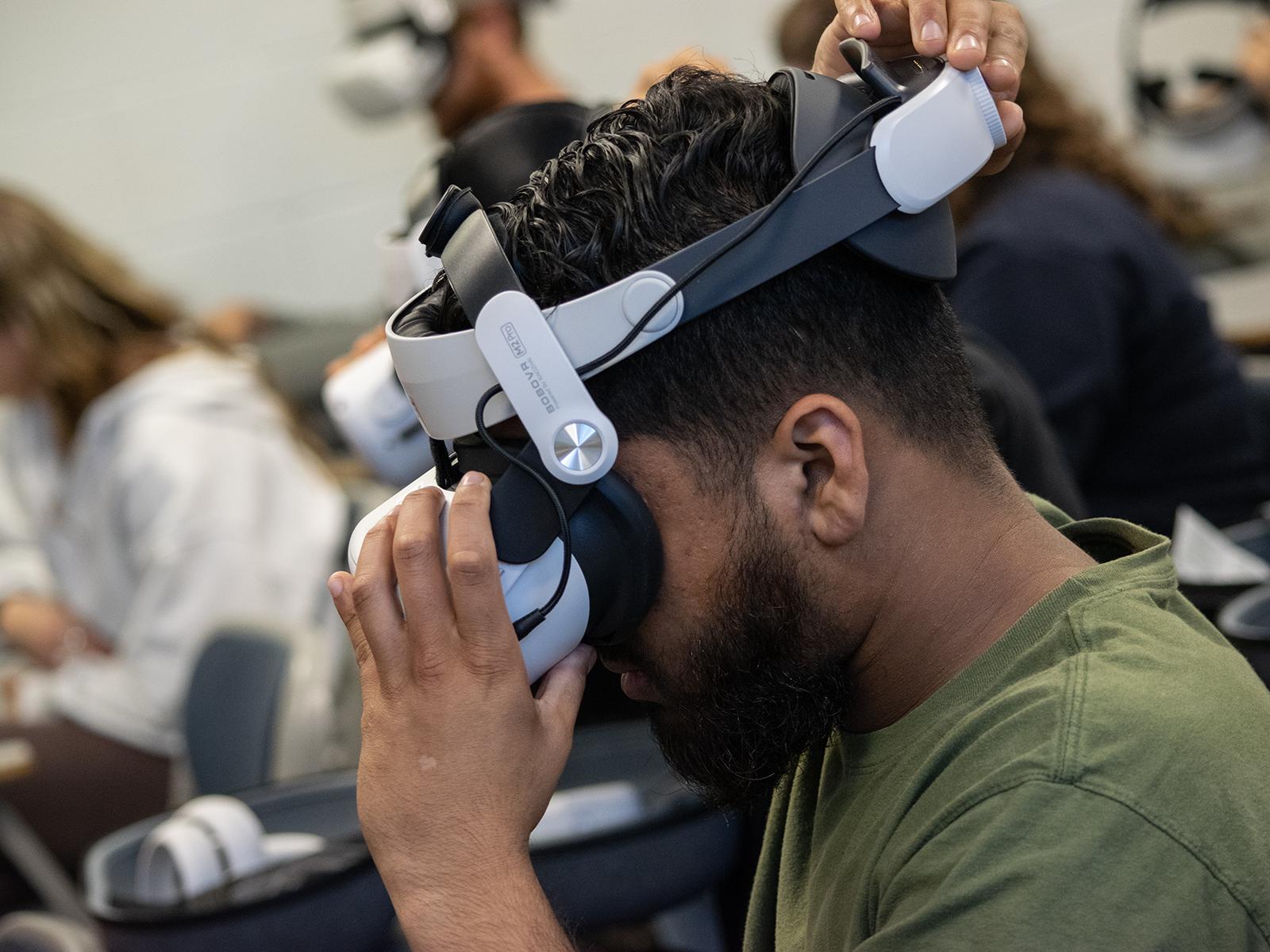 A student adjusts a virtual reality headset that is strapped to his head