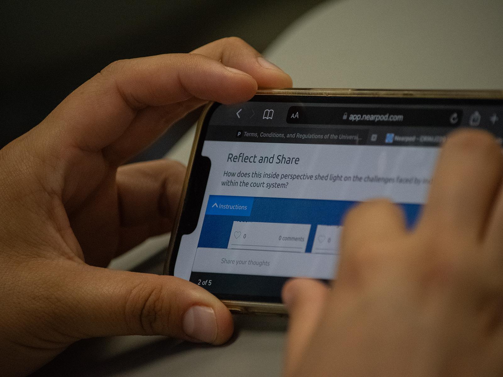Closeup of a student's hands holding a phone with a reflection question on the screen