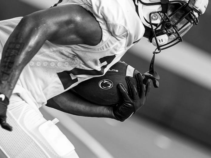 football player running with Penn State logo on football