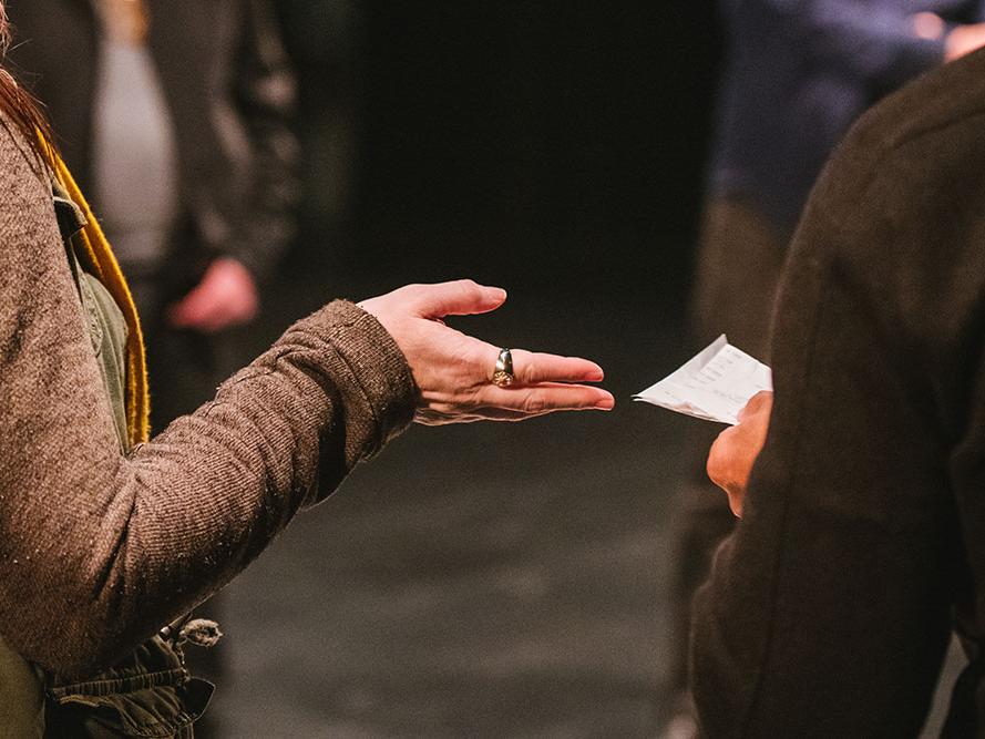 A cropped image shows the arm and hand of one person passing a notecard to another person.