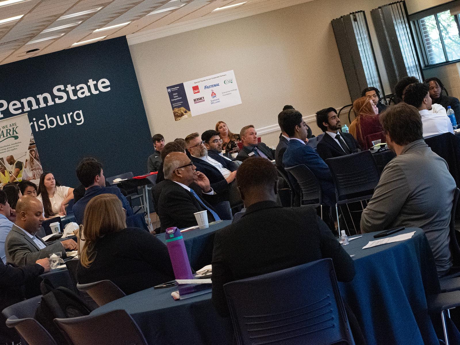 People sitting at round tables listen to a keynote speaker