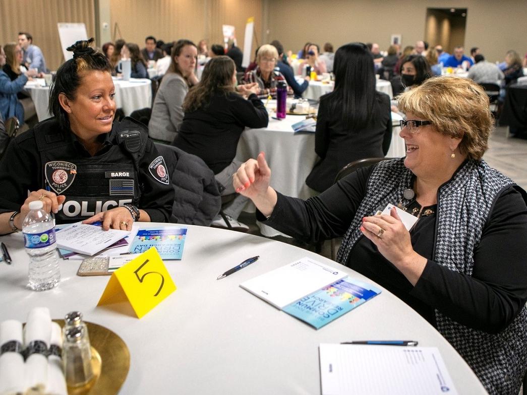 Two women, one wearing a police uniform, sit together and have a conversation. 