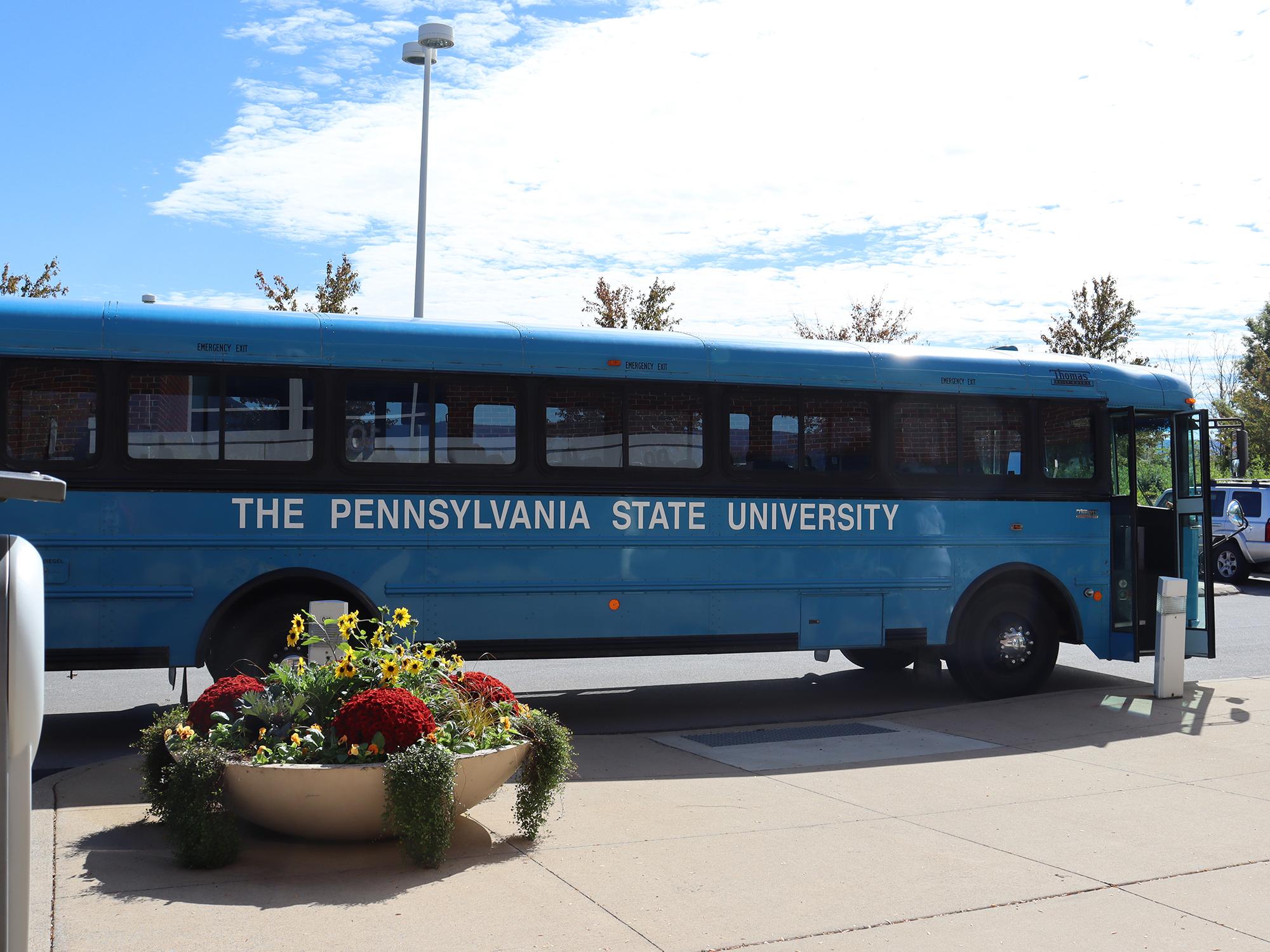 A blue bus pulls up to a curb in a parking lot.Members of the Homecoming Court traveled to different homecoming events on an iconic Penn State blue bus.
