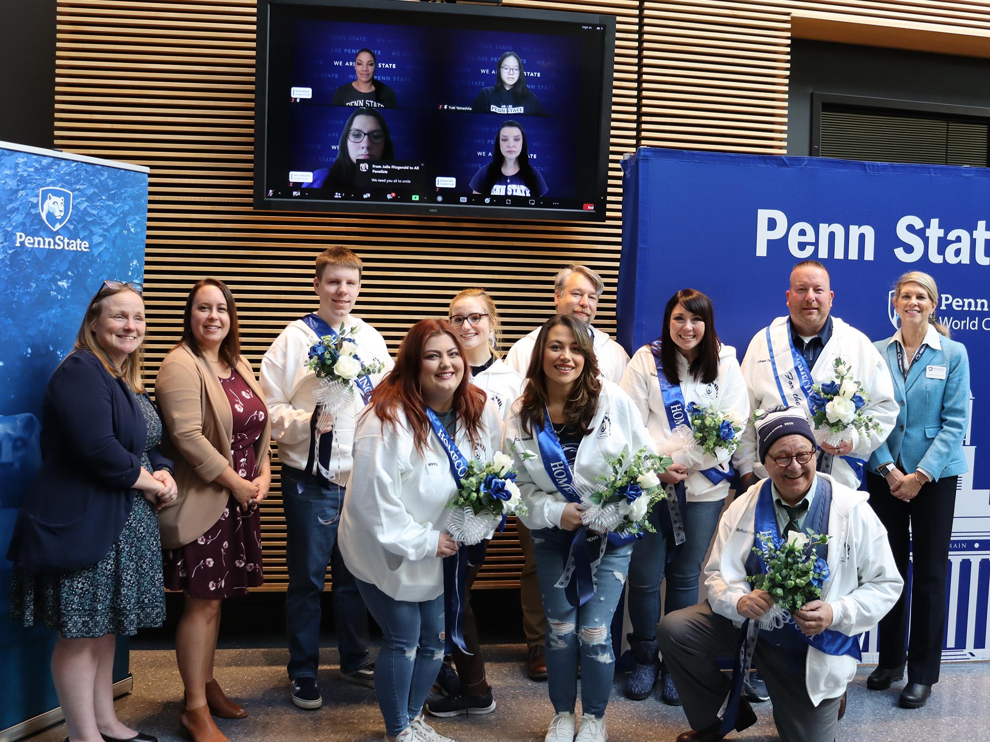 A group of people stand together in front of a TV screen.