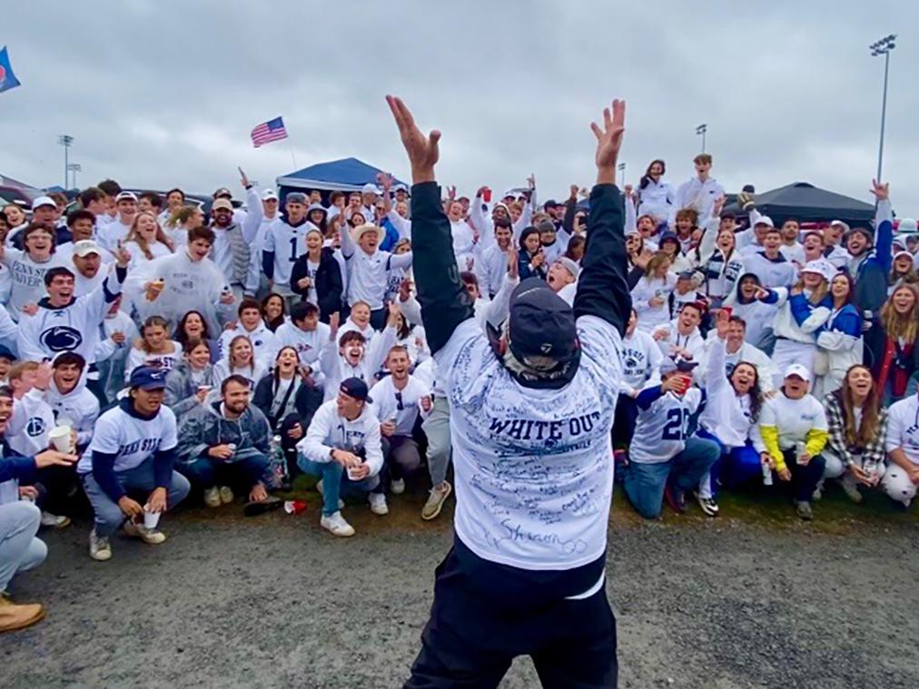 Dale Quayle raises his arms to lead a cheer from the dozens of people at the tailgate.