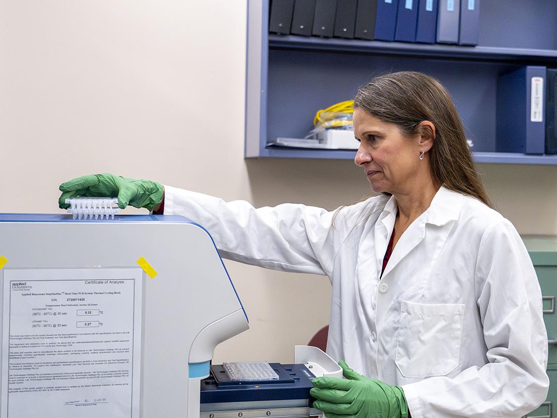 Person in a lab coat stands in front of a machine.