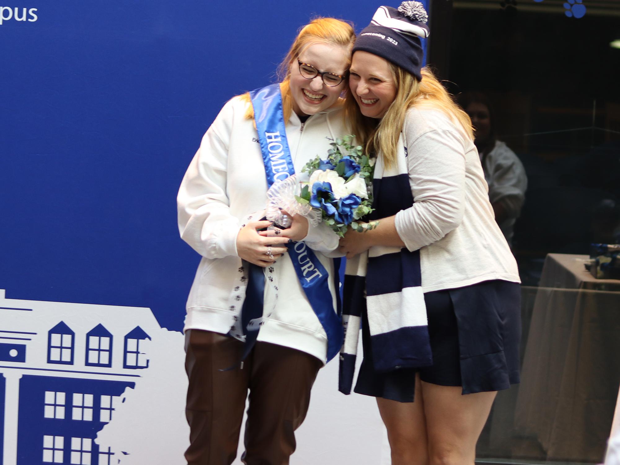 Two women hug in front of a blue background.