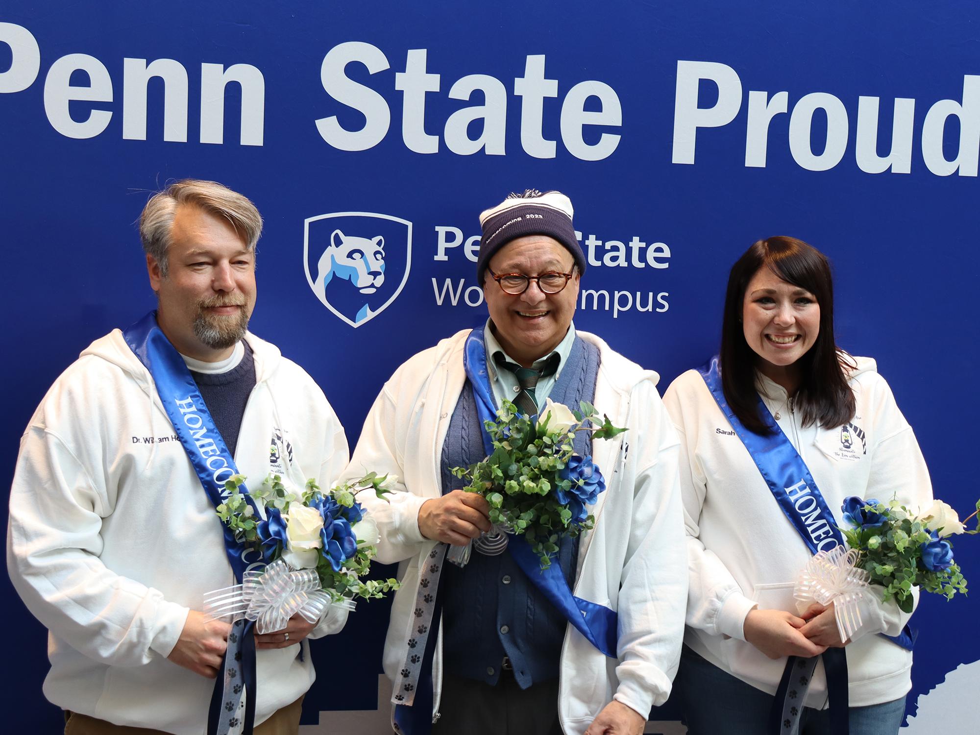 Three people pose for a photo in front of a blue background.