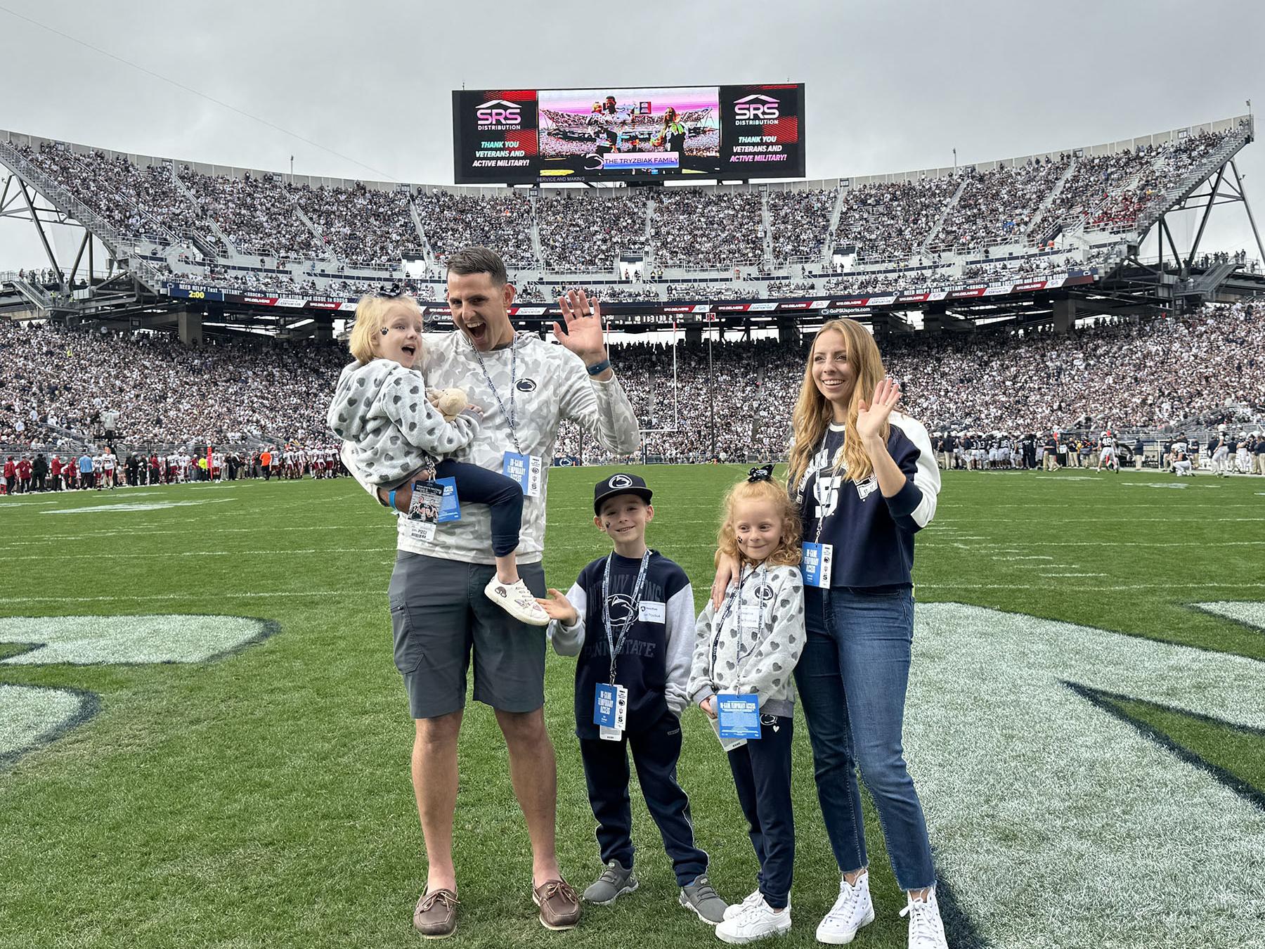A man, woman and three children stand and wave on a football field.