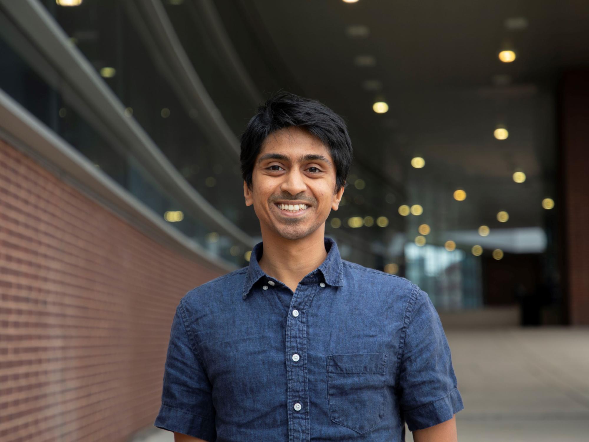smiling dark-haired person in blue button-down shirt 