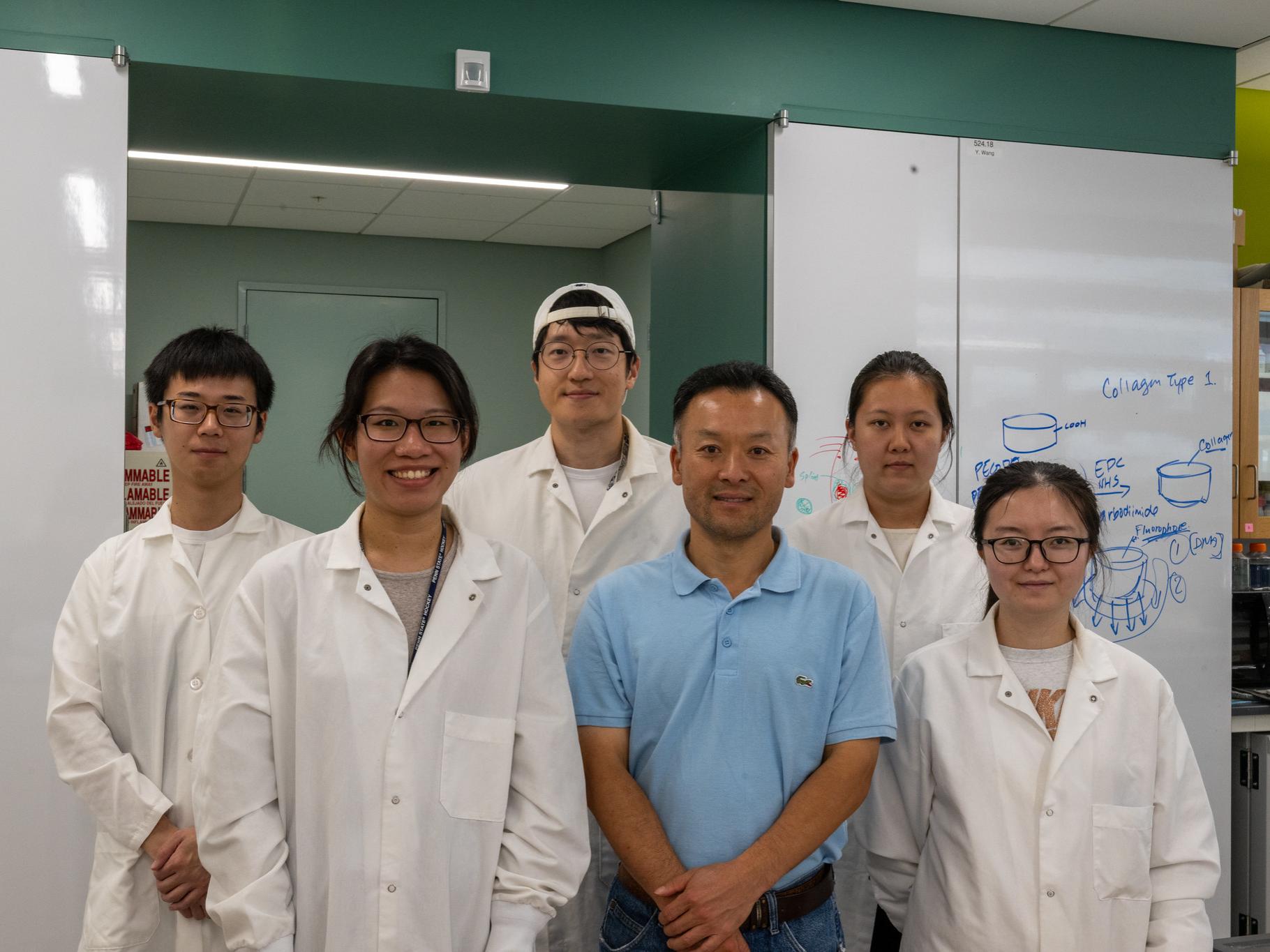 six people in a laboratory stand next to each other as they pose for a photo