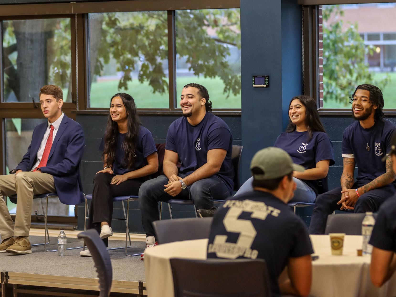 Five students sit in a line of chairs 