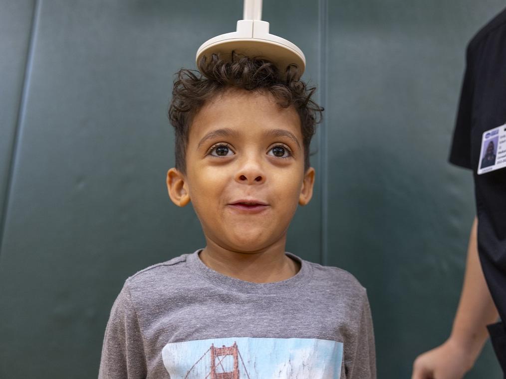 A little boy stands as a health care worker puts a disk on top of his head to measure his height.