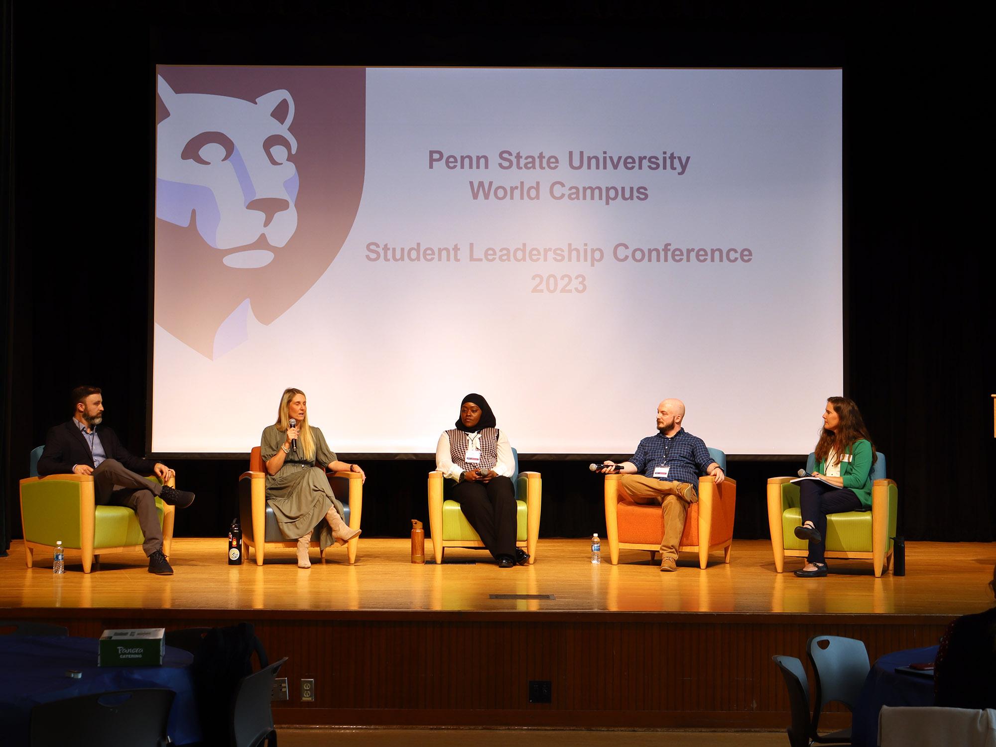 A group of alumni sit on chairs on a stage