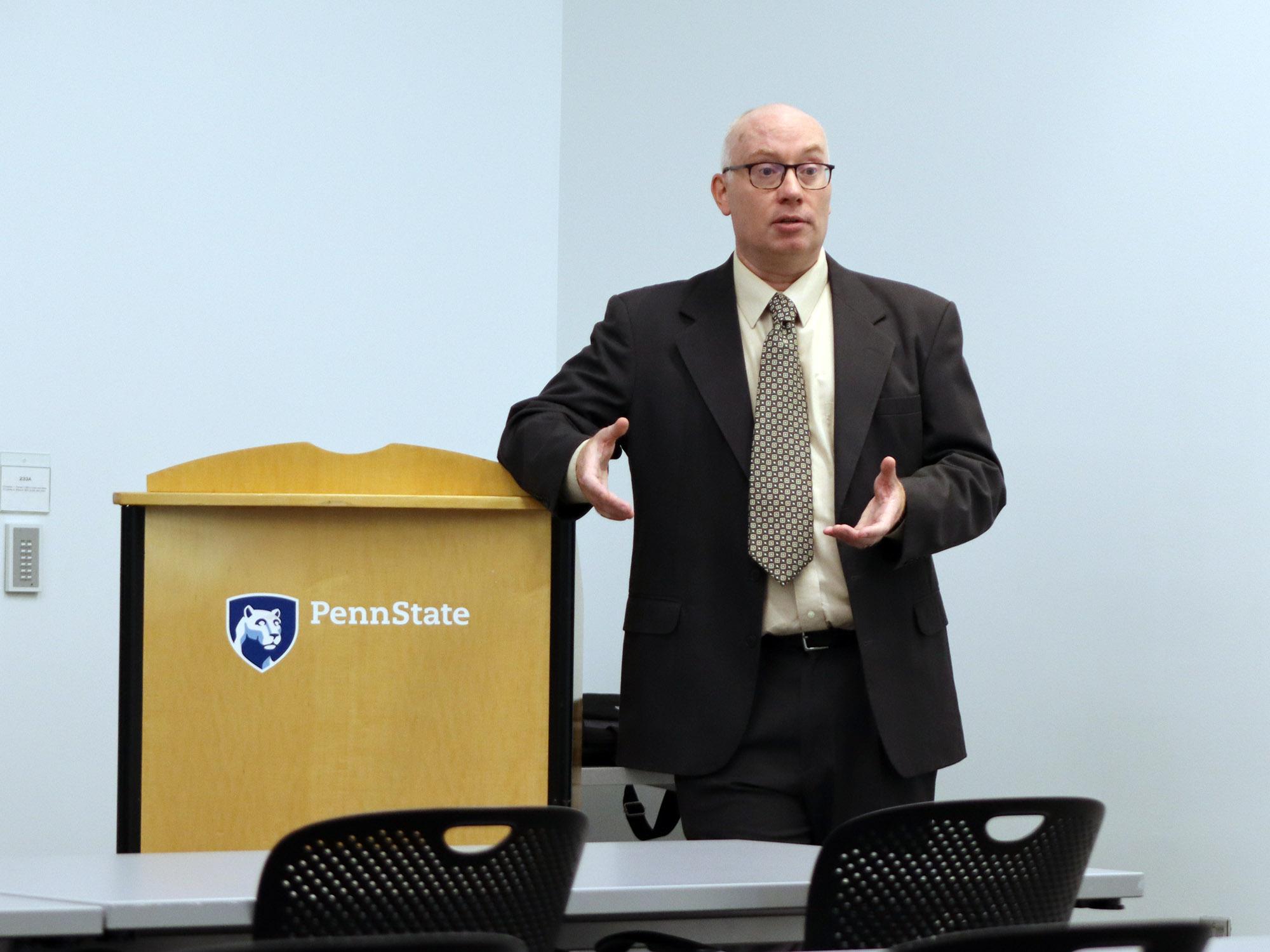 A professor stands next to a podium addressing a group